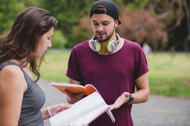 person-talking-with-friend-and-holding-book-in-park
